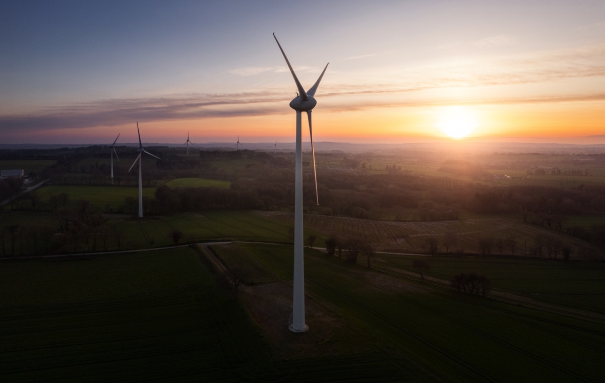 Coucher de soleil sur un paysage rural avec plusieurs éoliennes en activité illustrant une production d'énergie renouvelab