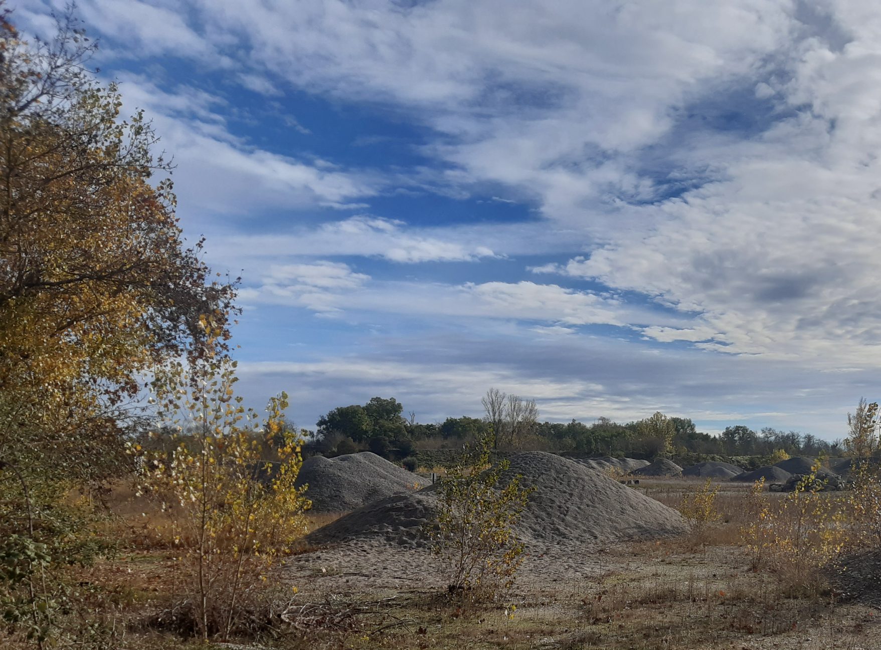 Paysage naturel en automne avec terrain de gravier et végétation clairsemée sous un ciel dégagé
zone de carrières aband