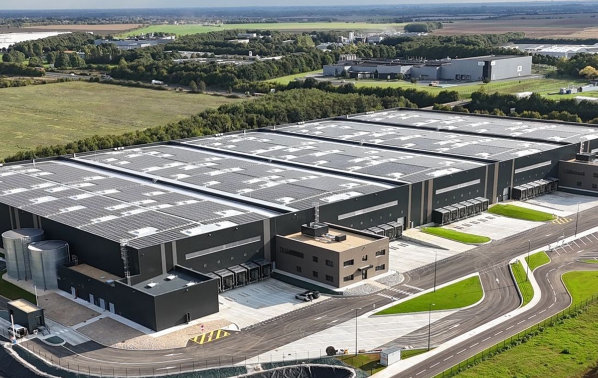 Vue aérienne d'un vaste complexe industriel moderne avec des bâtiments équipés de toitures photovoltaïques dans un cadre