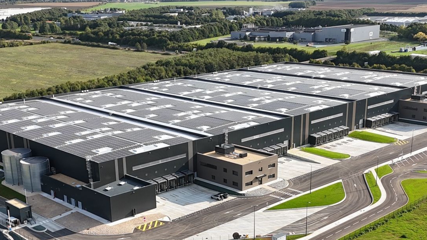 Vue aérienne d'un vaste complexe industriel moderne avec des bâtiments équipés de toitures photovoltaïques dans un cadre